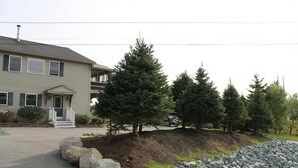 A two-story building with a front porch, a driveway, and a landscaped area with rocks and trees. - Modern Condo #1! (Ellsworth)