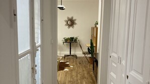Um corredor com piso de madeira, paredes brancas e luminária no teto. Há uma porta à esquerda e um armário à direita.
