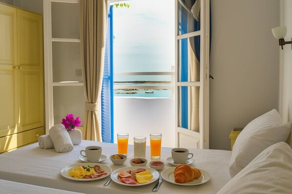 A neatly made bed with a breakfast table set with plates of food, drinks, and a vase of flowers.