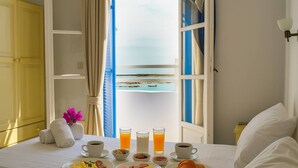 A neatly made bed with a breakfast table set with plates of food, drinks, and a vase of flowers. - Beachfront Bocamviglies Room - Naoussa Sunny Suite (Naoussa)