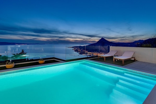 A rooftop infinity pool with a view of a city and a mountain at dusk.
