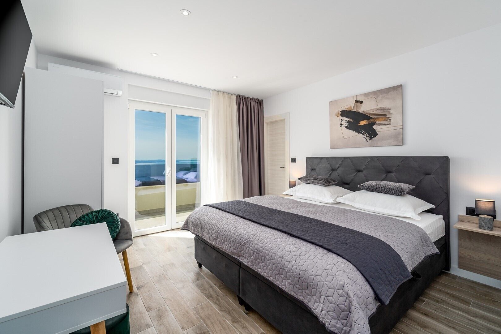 Ein modernes Schlafzimmer mit einem großen Bett, einem Schreibtisch und einem Balkon mit Blick.