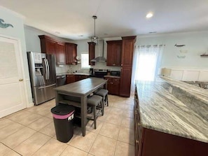 A kitchen with a central island, dark wooden cabinets, stainless steel appliances, and a tiled floor.