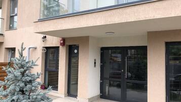 A building with a modern design, featuring a glass balcony, a door with a glass panel, and a small tree in front.