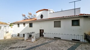 Un bâtiment blanc avec un toit recouvert de tuiles, une petite fenêtre et une clôture en métal.