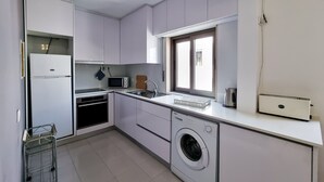 Une cuisine compacte avec des meubles blancs, un lave-linge, un four à micro-ondes et une petite fenêtre.