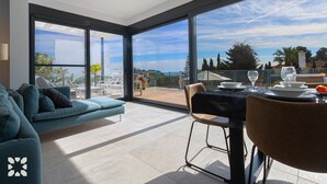Sala de estar moderna com uma grande parede de vidro, um sofá, uma mesa de jantar posta para dois e vista para o exterior.