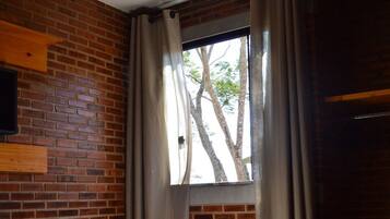 Una stanza con un letto, una finestra con tende, un muro in mattoni e una mensola di legno.