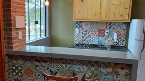 Una cocina con pared de ladrillo, ventana, salpicadero de azulejos, armarios de madera y dos taburetes de bar.