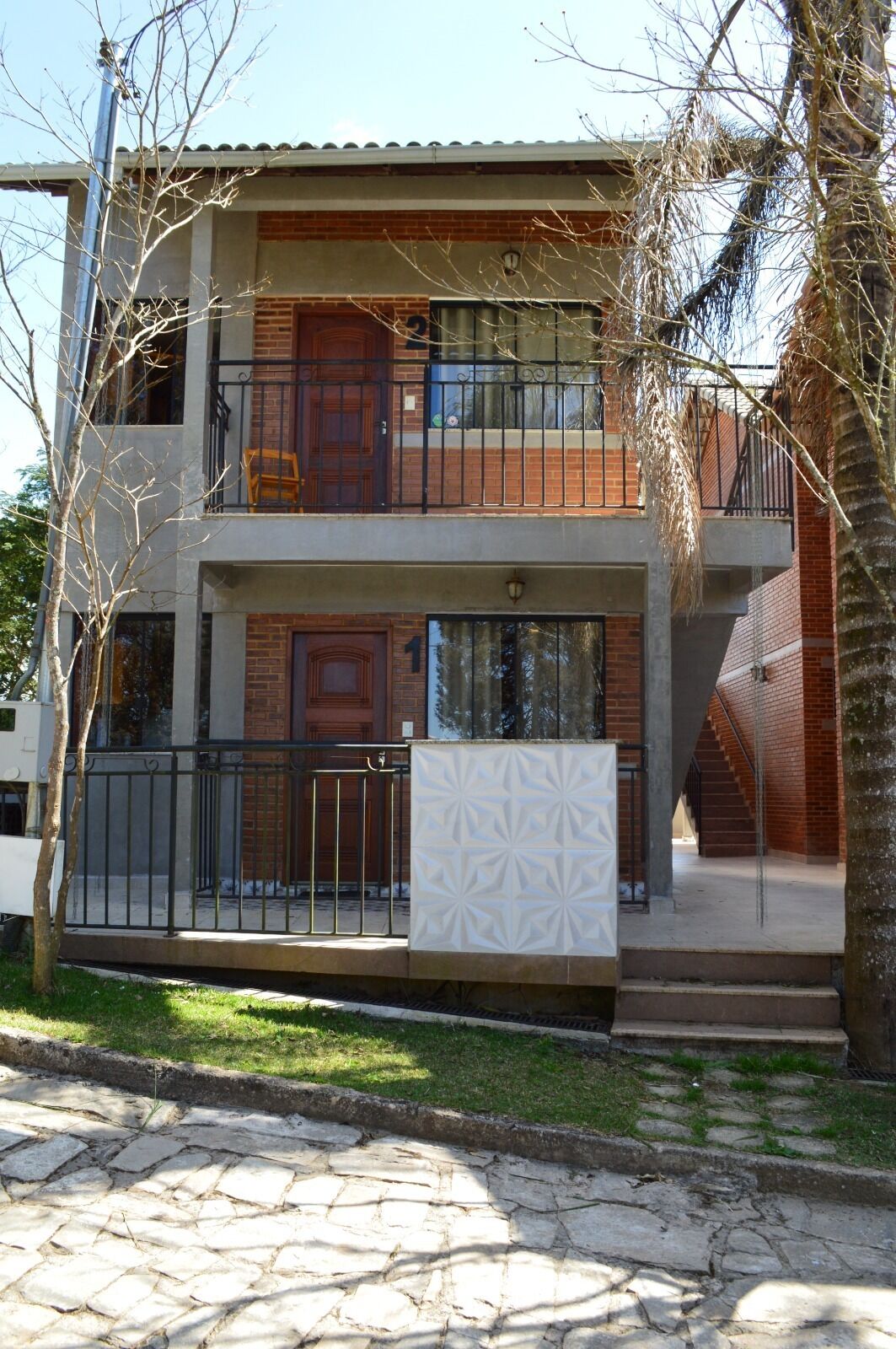 Un bâtiment à deux étages, doté d’une façade en briques, d’un balcon à l’étage supérieur et d’un escalier menant à l’entrée.
