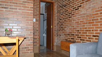 Una habitación con pared de ladrillo, una mesa de madera con un florero, un sofá gris y una puerta que da a otra estancia.