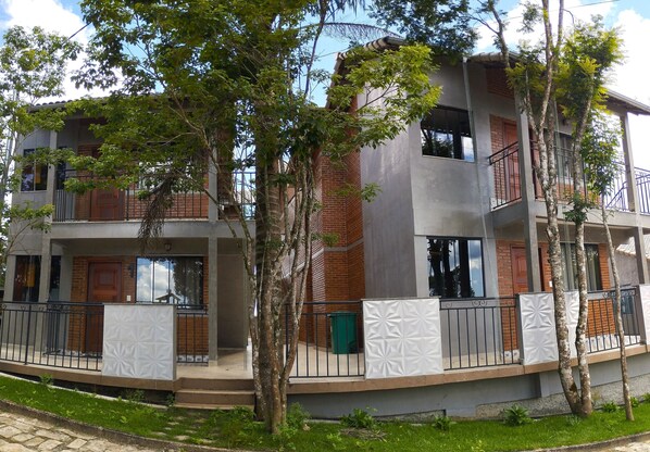 A multi-story residential building with a balcony, brick facade, and surrounding greenery.