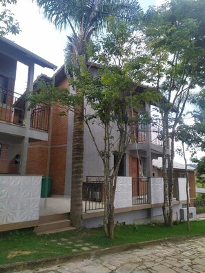 A two-story building with a brick facade, balconies, and a grassy area in front.