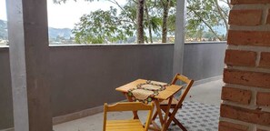 A balcony with a table and chairs, a brick wall, and a view of trees and mountains.