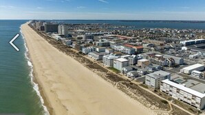 Luftaufnahme einer Küstenstadt mit Strand, dichter Wohnbebauung und einem Yachthafen.