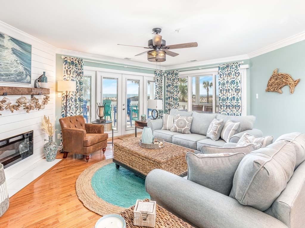 A living room with a fireplace, a ceiling fan, a sofa, a coffee table, and patterned curtains.