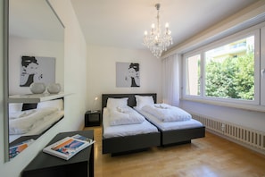 Ein Schlafzimmer mit zwei Betten, einer Kandelaber, einem großen Fenster und Kunstwerken an den Wänden.