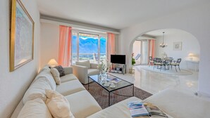 Ett modernt vardagsrum med en soffa, ett soffbord, en tv och en matplats med stolar och ett bord.