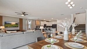 Ein modernes Wohnzimmer mit grauem Sofa, einem Esstisch für sechs Personen und einer Küche im Hintergrund.