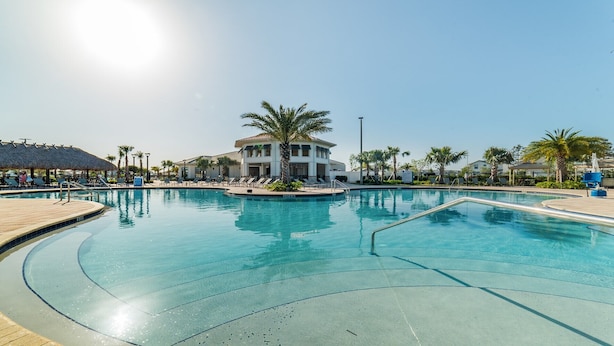 Ein großer Pool mit Liegestühlen und Palmen, umgeben von Gebäuden und einem klaren Himmel.