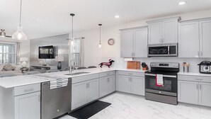 Una cocina moderna con gabinetes grises, electrodomésticos de acero inoxidable, una isla central y una zona de comedor con sofá y mesa.