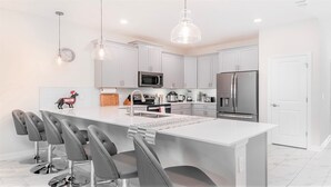 Una cocina moderna con gabinetes blancos, electrodomésticos de acero inoxidable y una isla central con taburetes de bar.