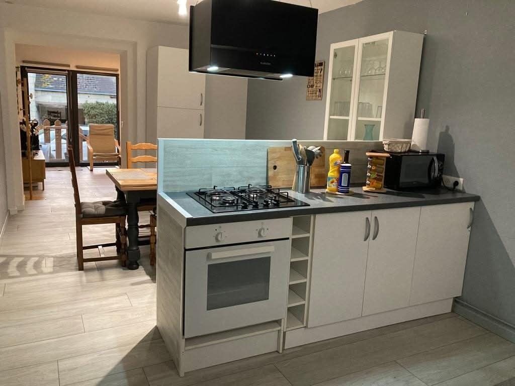 Een compacte keuken met een gasfornuis, oven en een magnetron. Door een open deur is een eethoek met een tafel en stoelen zichtbaar.