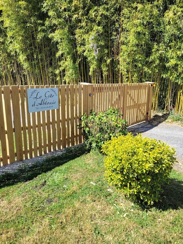 Une clôture en bois avec un panneau, un petit buisson et, au fond, une forêt de bambous.