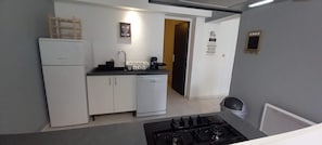 Une cuisine compacte équipée d’un réfrigérateur, d’un évier et d’une cuisinière. On y trouve également un petit placard et une machine à café sur le plan de travail.