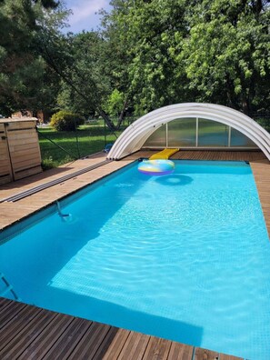 A swimming pool with a wooden deck and a covered area.