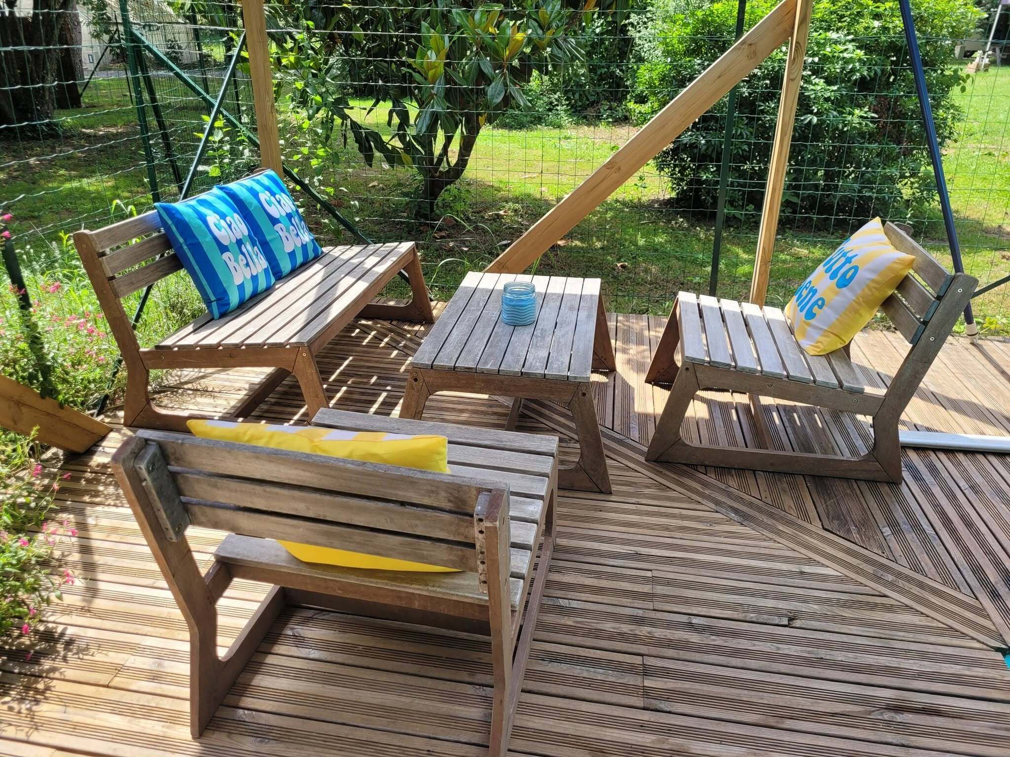A wooden deck with three wooden chairs and a table, surrounded by a wire fence and greenery.