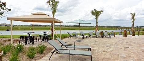 Zona de patio con sillones, mesas y sombrillas, con vista a una masa de agua.