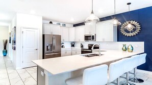 A modern kitchen with white cabinets, stainless steel appliances, a large island with bar stools, and pendant lighting. - Last Minute Disney! Private Pool, Hot Tub, Game Room & Themed Bedrooms. Book Now! #56475 (Orlando)
