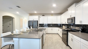 A modern kitchen with white cabinets, a black countertop, stainless steel appliances, and a central island with seating.