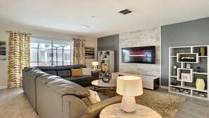 A modern living room with a sectional sofa, a TV mounted on the wall, and a decorative shelf unit.