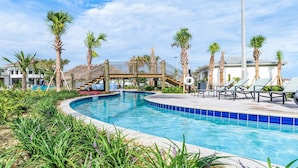 A swimming pool with a curved edge, surrounded by palm trees and a wooden deck with lounge chairs.
