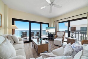 Ein geräumiges Wohnzimmer mit einem Glastisch, bequemen Sitzgelegenheiten, einem Deckenventilator und einem großen Fenster mit Meerblick.