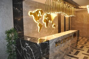 A reception desk with a world map illuminated in gold, a modern chandelier, and a marble floor with a geometric pattern. - Golaz Suit Otel (Ankara)