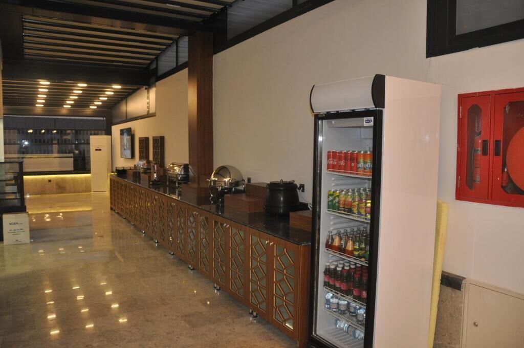 A hotel lobby with a reception desk, a refrigerator stocked with beverages, and a fire extinguisher on the wall.