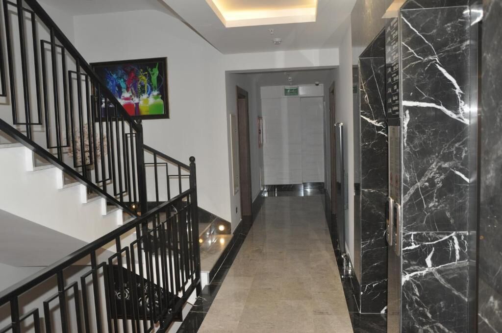 A modern hotel lobby with a marble staircase, a flat-screen TV, and a hallway leading to a door.