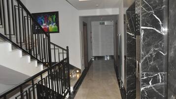 A modern hotel lobby with a marble staircase, a flat-screen TV, and a hallway leading to a door.