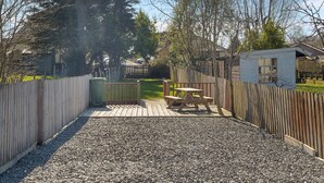 Ein Garten mit einer Holzterrasse, einem Picknicktisch und einem Gartenhaus.