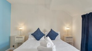 Ein ordentlich gemachtes Bett mit weißen Leinentüchern und zwei blauen Kissen, begleitet von Nachttischen mit Lampen, in einem Zimmer mit hellblauen Wänden.