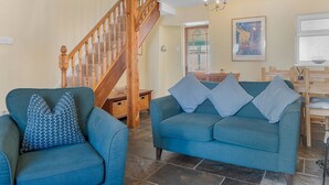 Ein Wohnzimmer mit einer Holztreppe, einem blauen Sofa und einem gemusterten Sessel.