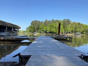Une jetée en bois s’étendant sur un lac paisible, entourée d’arbres verdoyants et sous un ciel bleu clair.