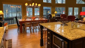 A spacious kitchen with a large island, wooden chairs, and a dining table. There are multiple windows providing natural light and views of the outdoors. - Reduced Spring rates! On Lake Oconee with Sunset Views, 2 Masters (Eatonton)