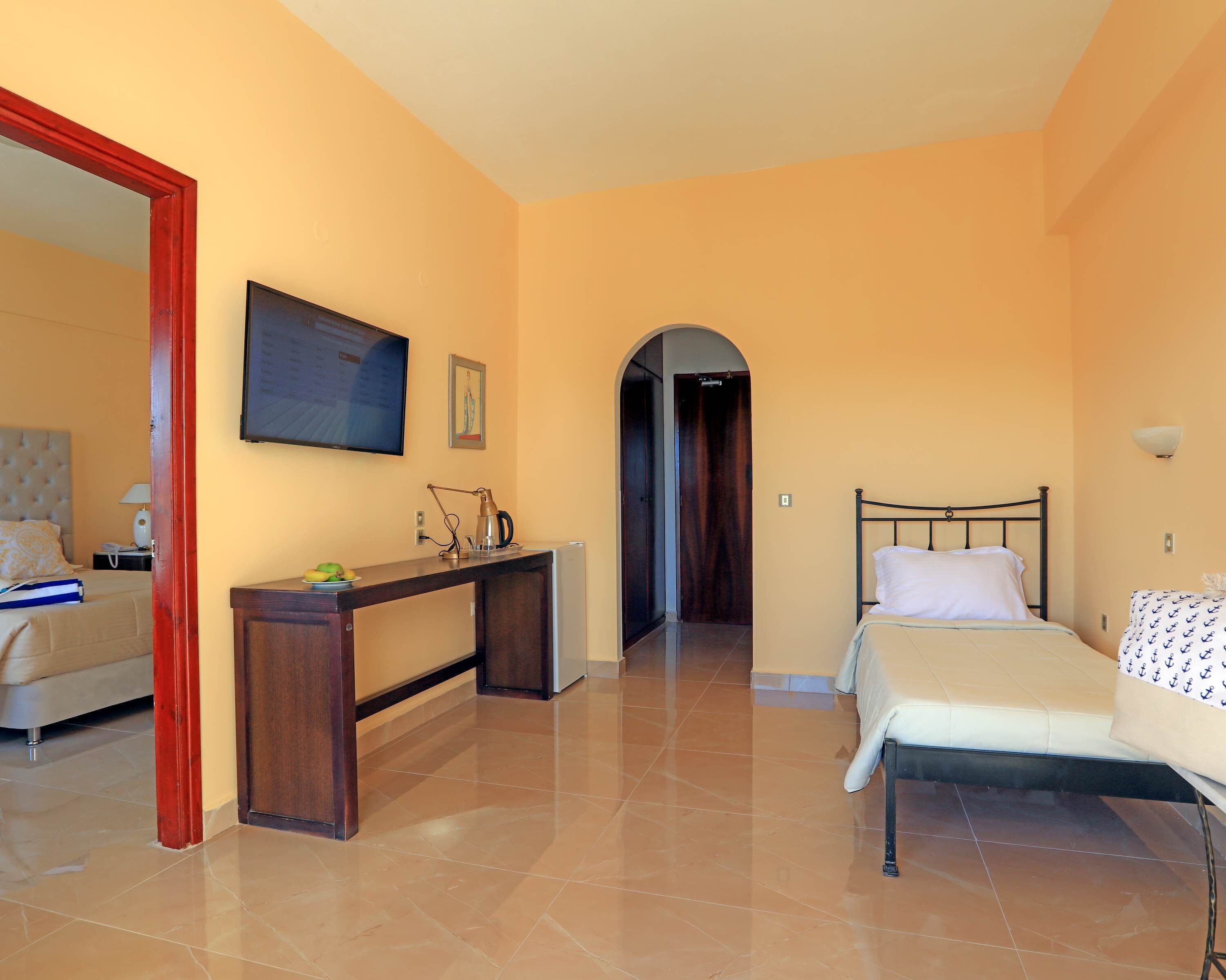 A hotel room with a bed, a desk, a television, and a door leading to another room.