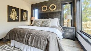 Een slaapkamer met een groot bed, twee aan de muur bevestigde kransen, een nachtkastje met een lamp en een raam met uitzicht op bomen.