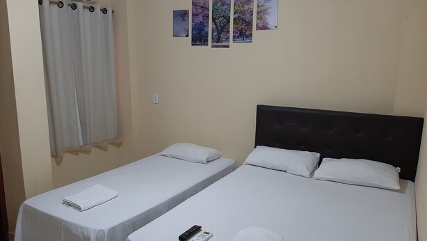 A hotel room with two single beds, a window with a curtain, and a wall with three framed pictures. - Hotel Rio Tapajós (Santarém)