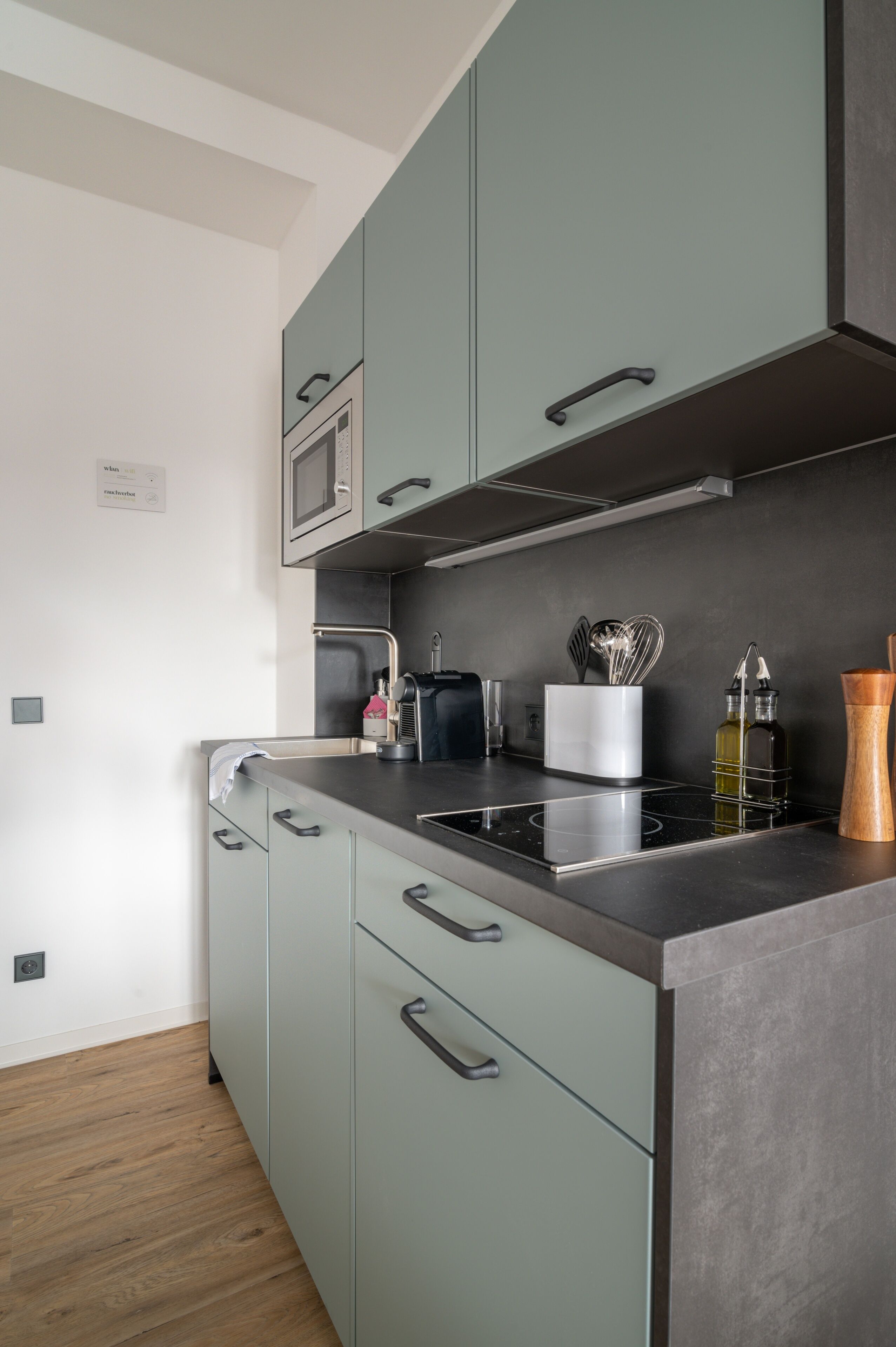 A modern kitchen with a built-in microwave, stainless steel countertop, and grey cabinets.